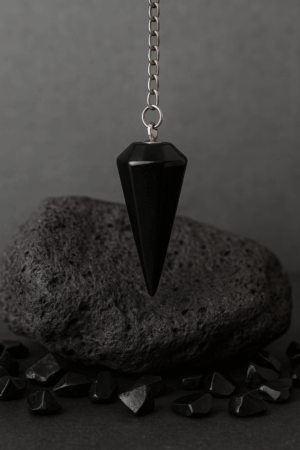 Εκκρεμές από Μαύρο Οψιδιανό πάνω σε ηφαιστειακή επιφάνεια με σκούρο μυστήριο φόντο και chips λίθου